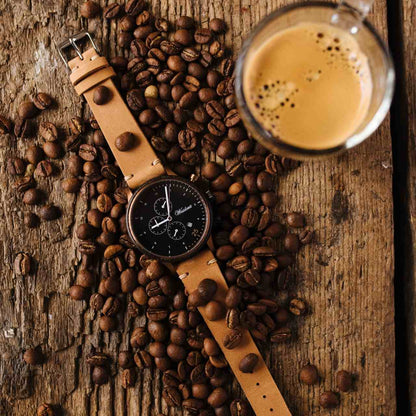 Drevené hodinky Waidzeit Barista Espresso Leather pri kávových zrnách – štýlové pánske hodinky z močiarného duba s čiernym chronografickým ciferníkom, bronzovými detailmi a koženým remienkom, zachytené v prostredí plnom vône čerstvo upraženej kávy